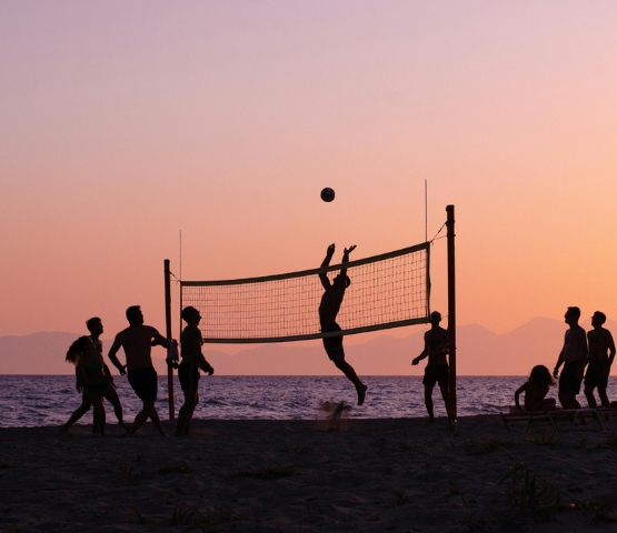 Groupe de personnes jouant au beach-volley sur la plage au coucher du soleil, en silhouette face à la mer
