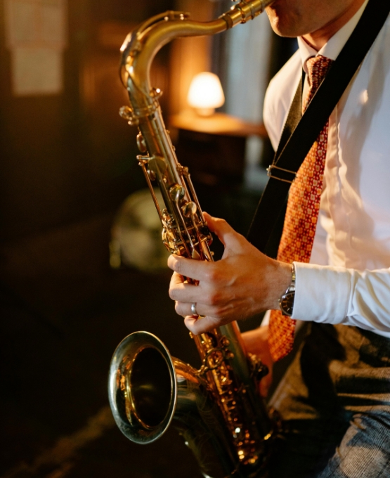 Musicien jouant du saxophone dans une ambiance chaleureuse en intérieur, vêtu d’une chemise et d’une cravate