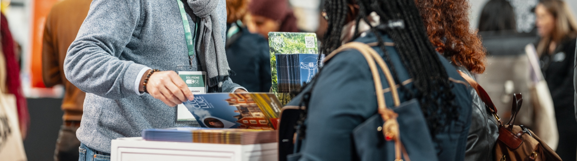 Exposant présentant une brochure à une participante sur un stand lors du salon Solutions CSE.