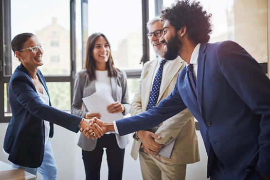 Participants en tenue professionnelle se serrant la main lors d’une rencontre, entourés de collègues souriants dans un environnement lumineux